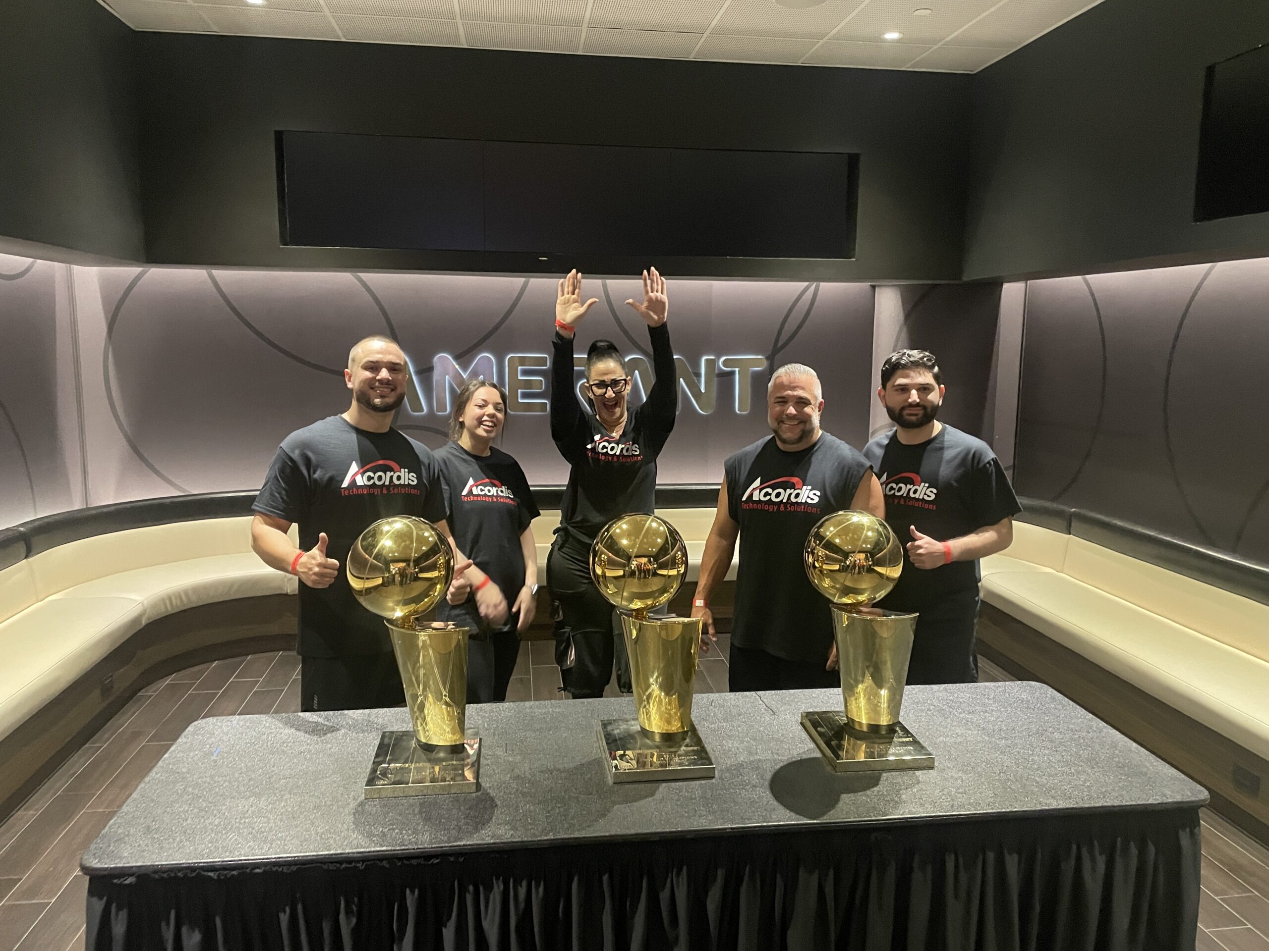 Four men celebrating with three NBA championship trophies on a table.